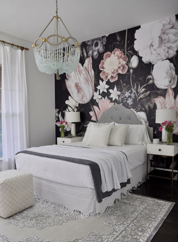 اتاق خواب با دیوارهای سفید و تخت پارچه ای تک نفره خاکستری که روی دیوار پشت تخت آن کاغذ دیواری سیاه با طرح گل های درشت نصب شده است